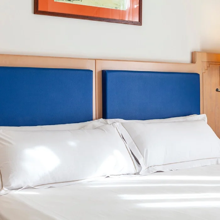 Cama con s&aacute;banas blancas y cabecero azul en una habitaci&oacute;n.