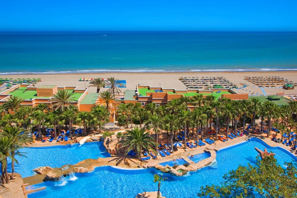 Vista aérea de un hotel frente al mar con piscina y palmeras