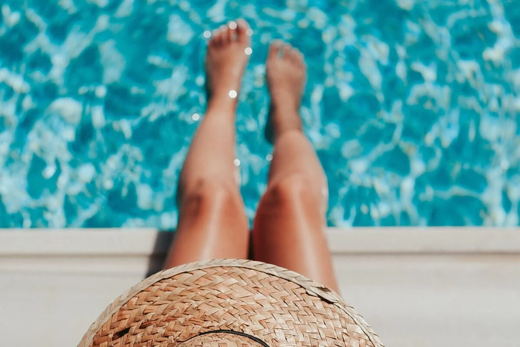 Pies descalzos en la piscina, enfocados con sombrero de paja en primer plano