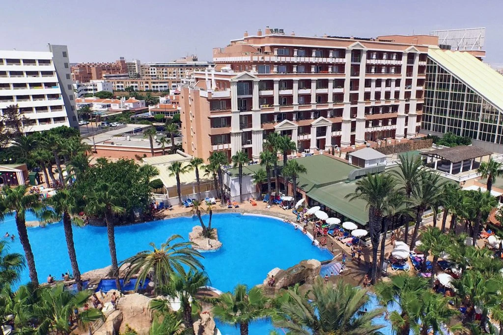 Hotel con piscina azul, palmeras y edificios en un entorno urbano tropical