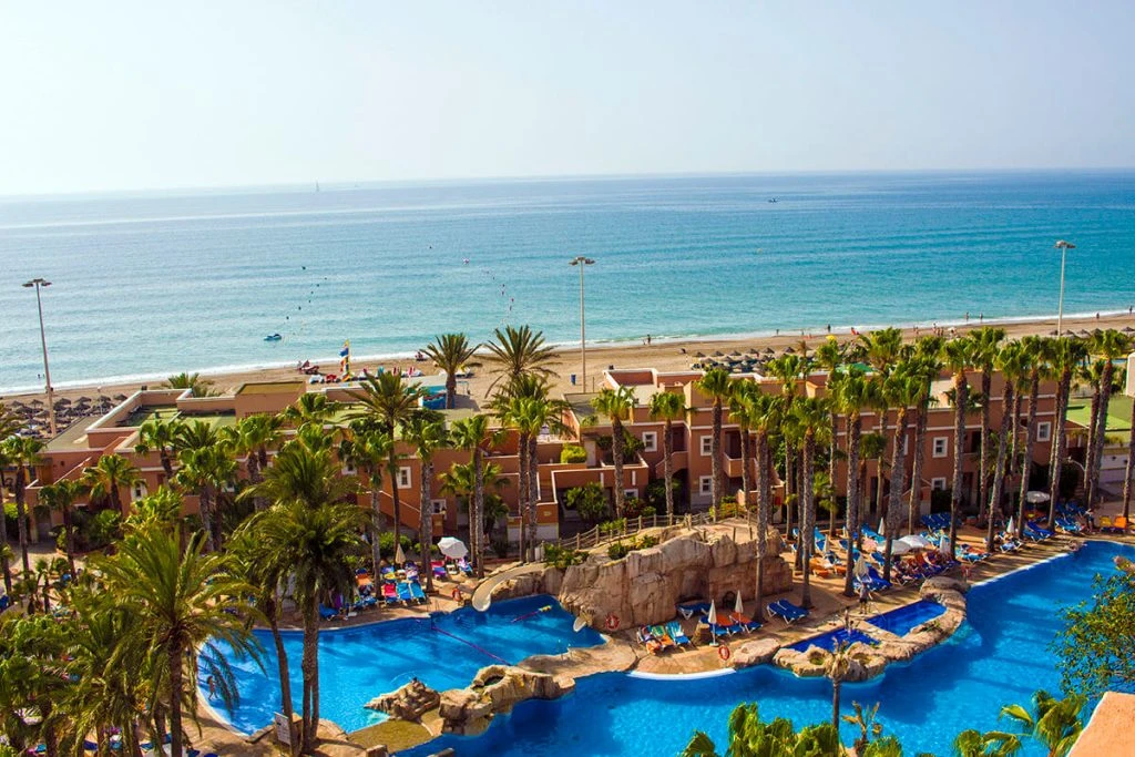 Hotel con piscina azul y palmeras frente al mar en la costa mediterránea