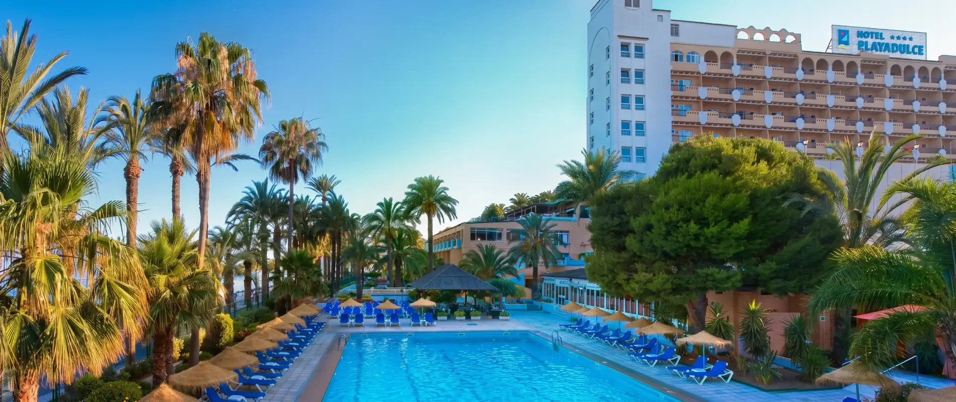 Piscina de hotel con palmeras y edificio &ldquo;Hotel Playadulce&rdquo; al atardecer