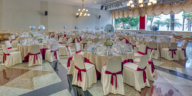 Sal&oacute;n de banquetes elegante con mesas redondas y sillas decoradas con mo&ntilde;os rojos.