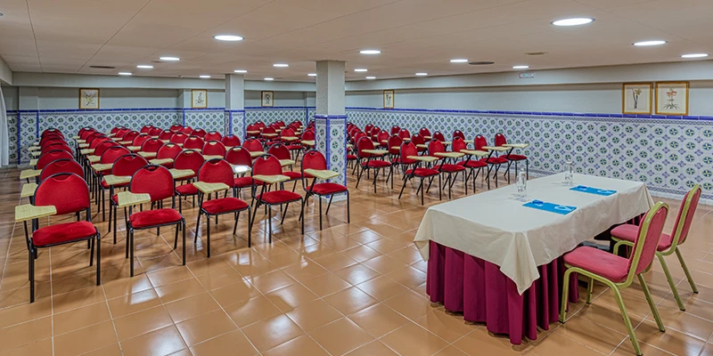 Sala de conferencias con sillas rojas y mesa cubierta de mantel blanco.