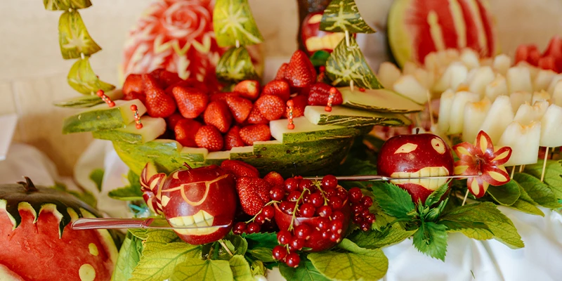 Frutas talladas y fresas decoran una bandeja con hojas y detalles frutales.