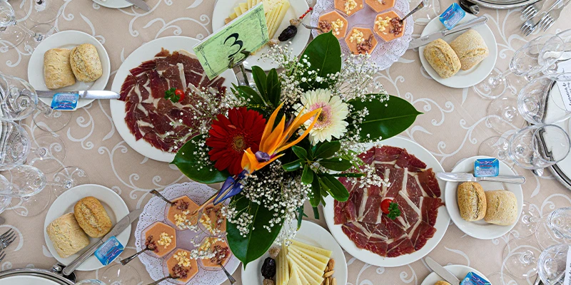 Mesa con platos de embutidos, queso, panecillos y un centro de flores.