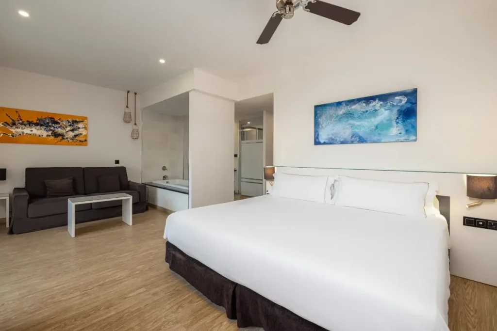 Habitaci&oacute;n de hotel moderna con cama blanca y cuadros de arte abstractos