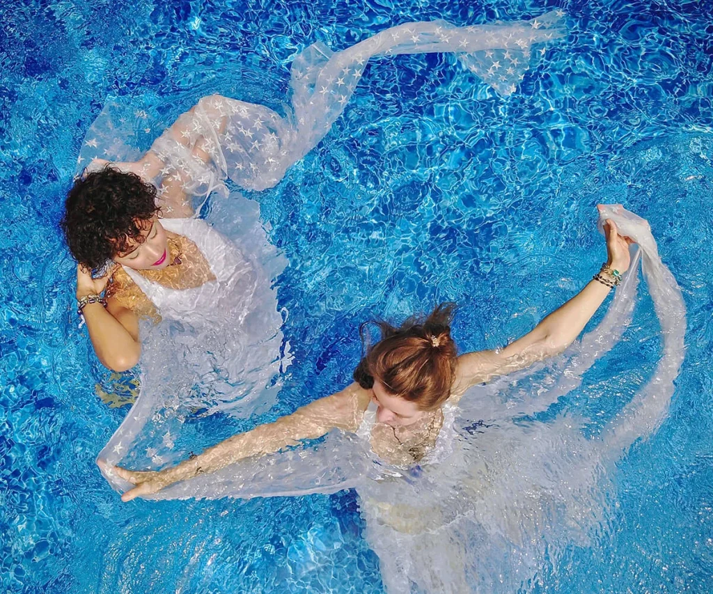Dos personas en piscina con tela transparente formando un coraz&oacute;n de nadadoras