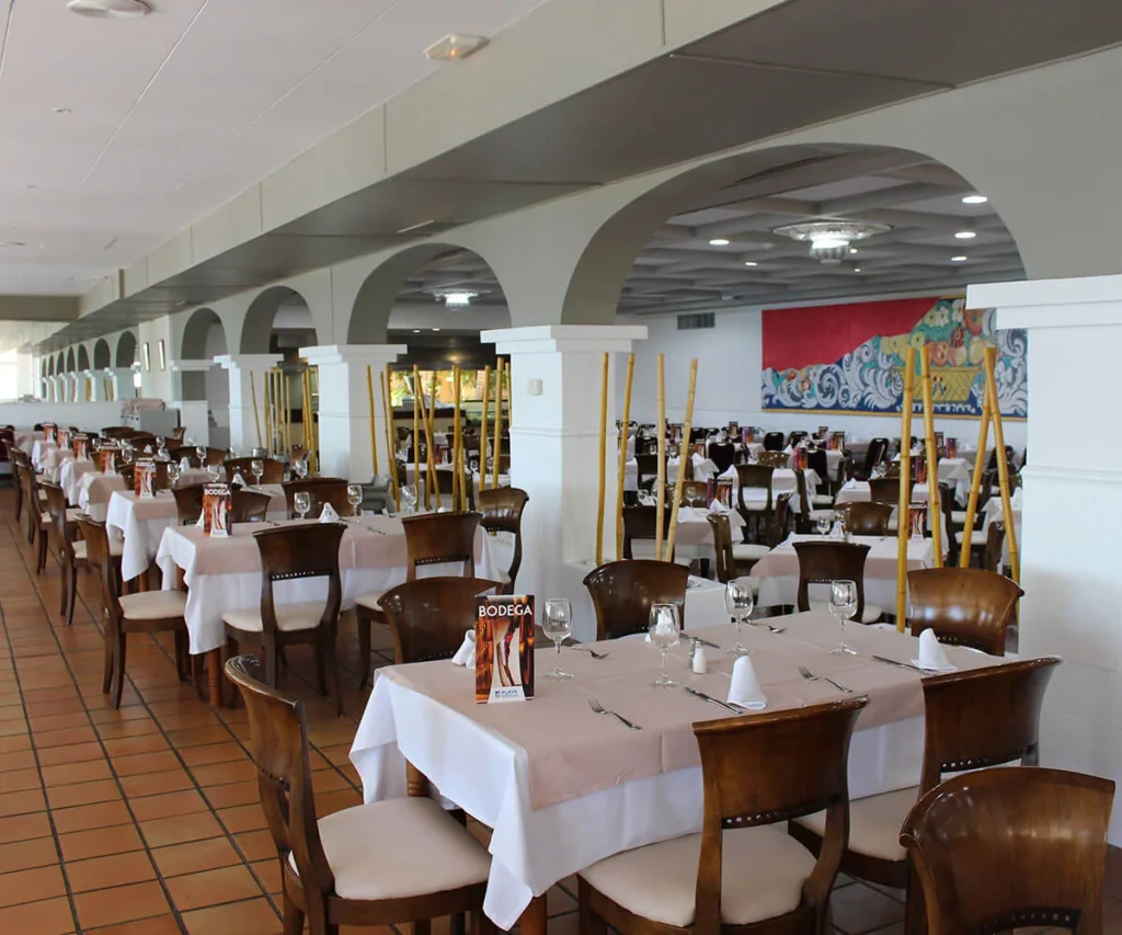 Comedor de restaurante con mesas servidas, sillas de madera y decoraci&oacute;n mural.