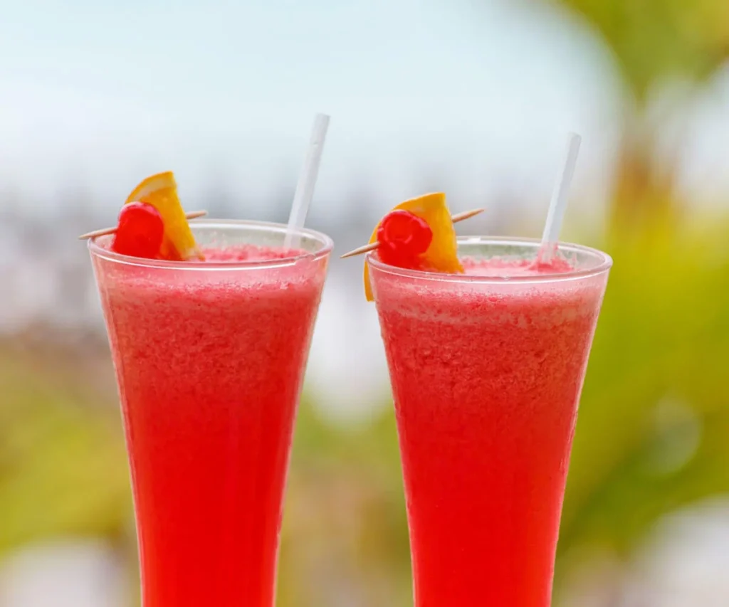 Dos vasos con bebida roja fr&iacute;a y palitos, con fruta en el borde.