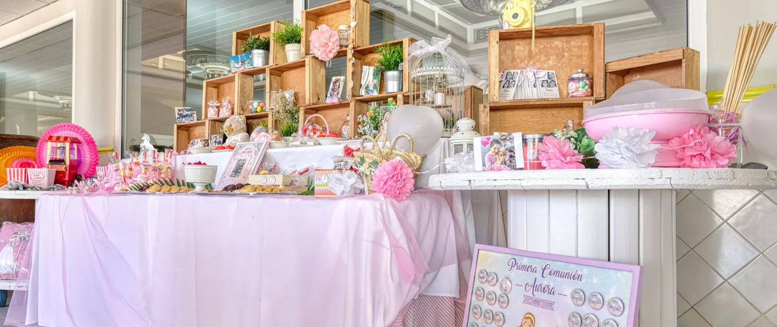 Mesa de dulces y decoraci&oacute;n rosa para primera comuni&oacute;n con regalos y flores.
