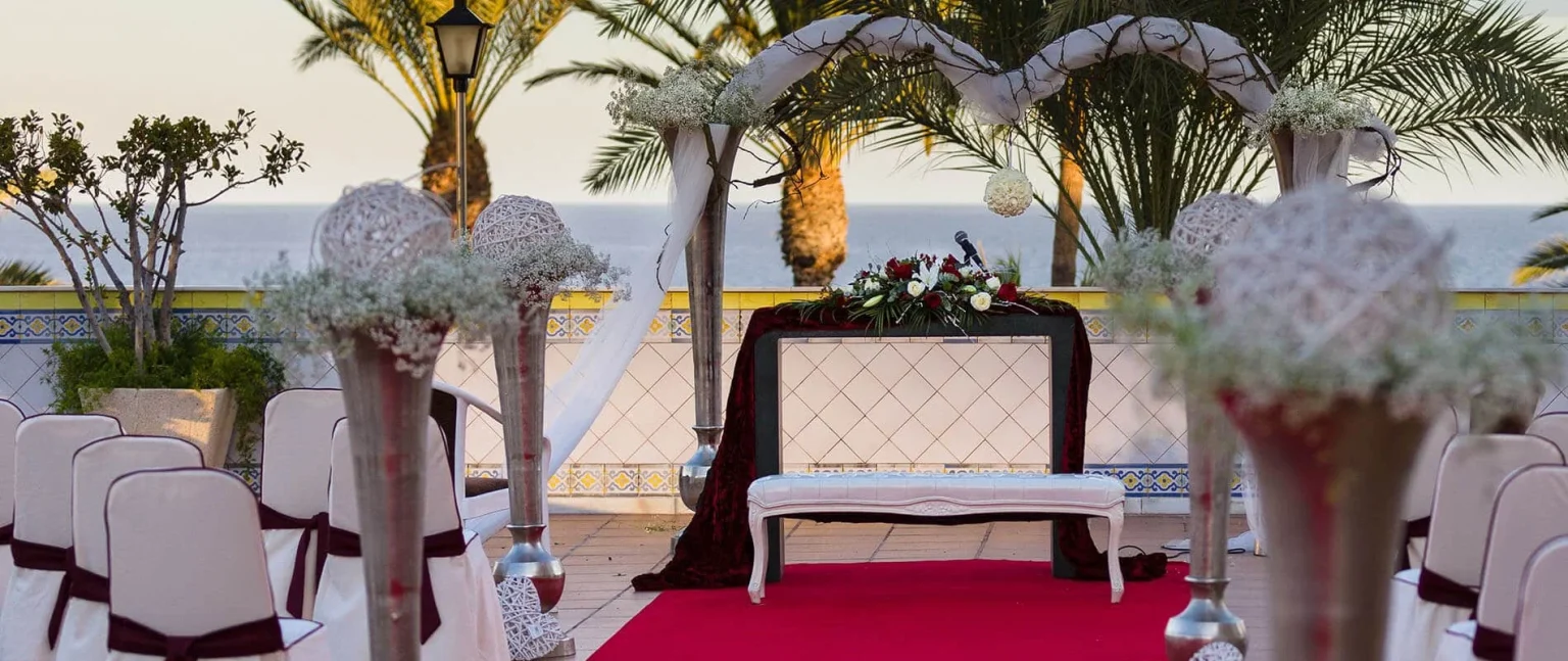 Boda al aire libre: arco y mesa con flores, escenario con cortinas rojas y sillas