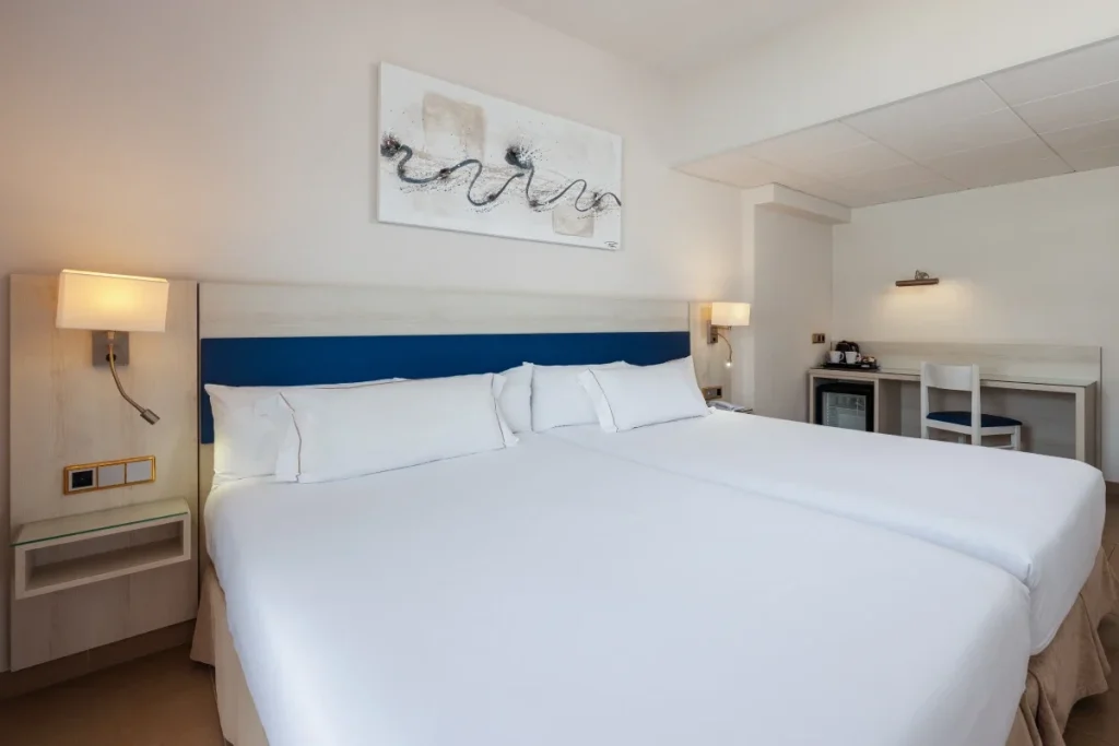 Habitaci&oacute;n de hotel con cama doble, l&aacute;mparas y mueble con minibar