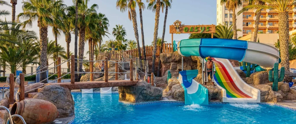 Tobogán azul en parque acuático con palmeras y piscina frente al hotel Oasis