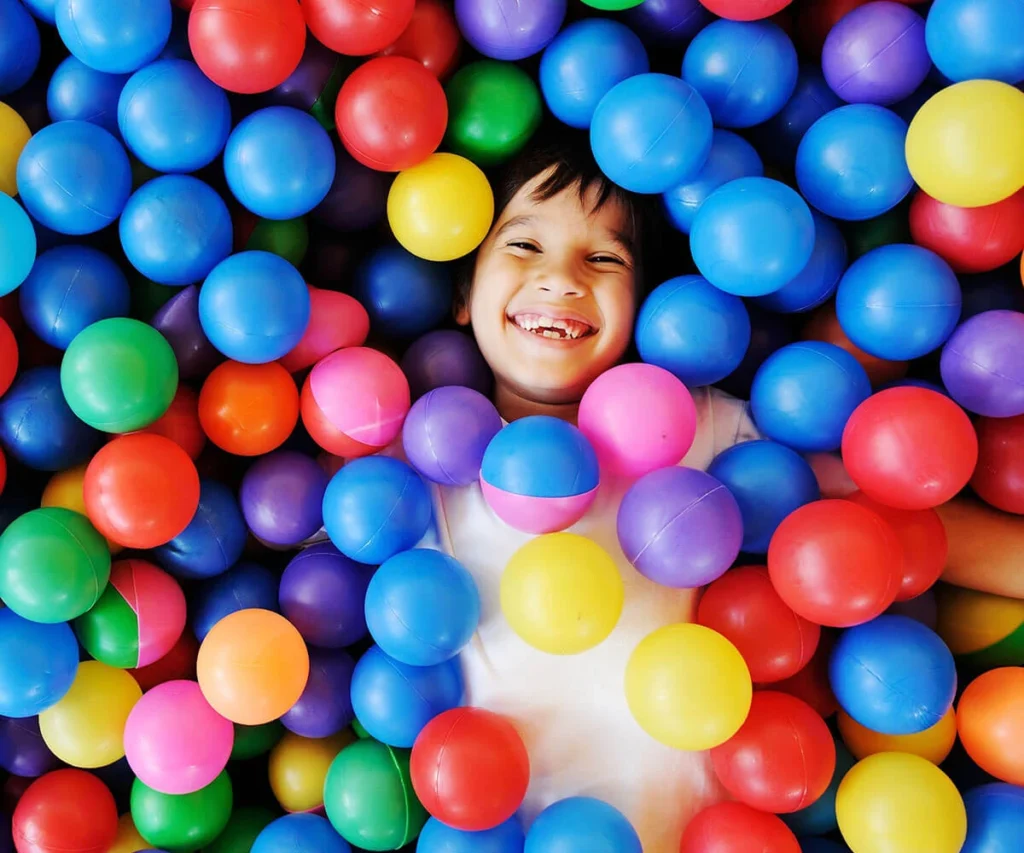 Ni&ntilde;o sonriente entre muchas pelotas de colores en un &aacute;rea de juegos