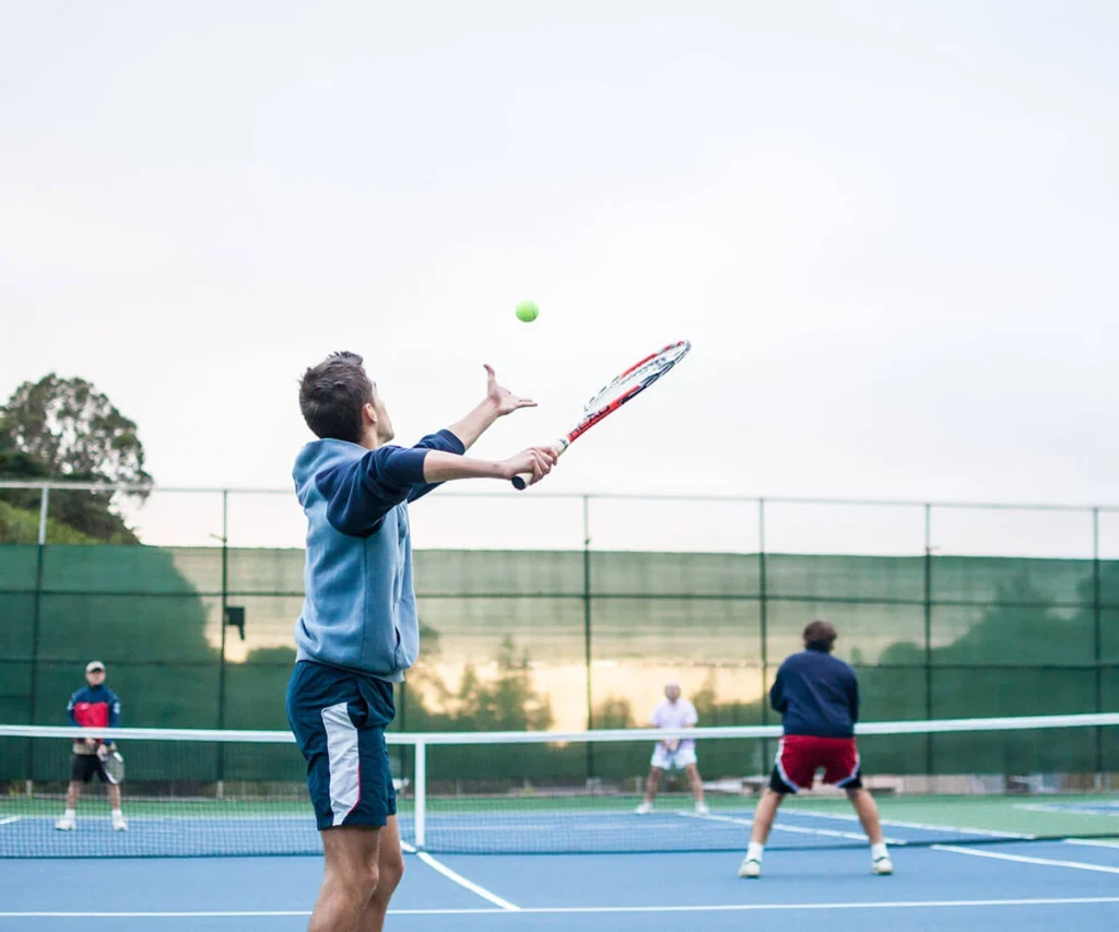 Jugador de tenis golpeando la pelota sobre una pista al atardecer