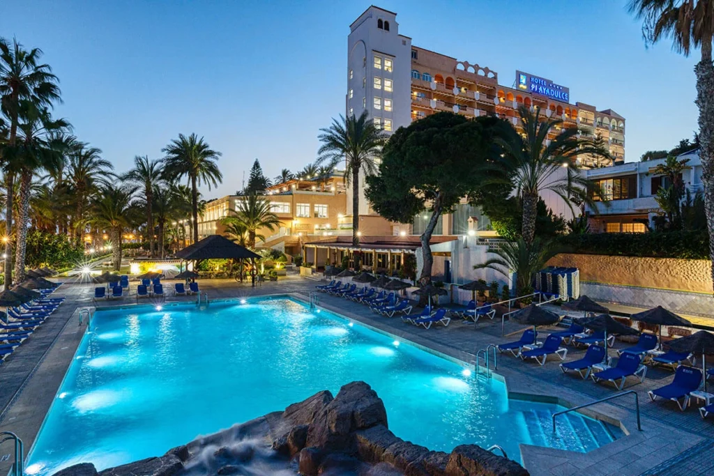Piscina azul con palmeras y fachada del Hotel Playa Adults Only al atardecer