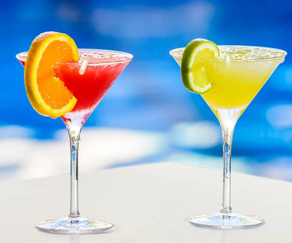 Dos c&oacute;cteles en copas: uno rojo con naranja, otro amarillo con lim&oacute;n.