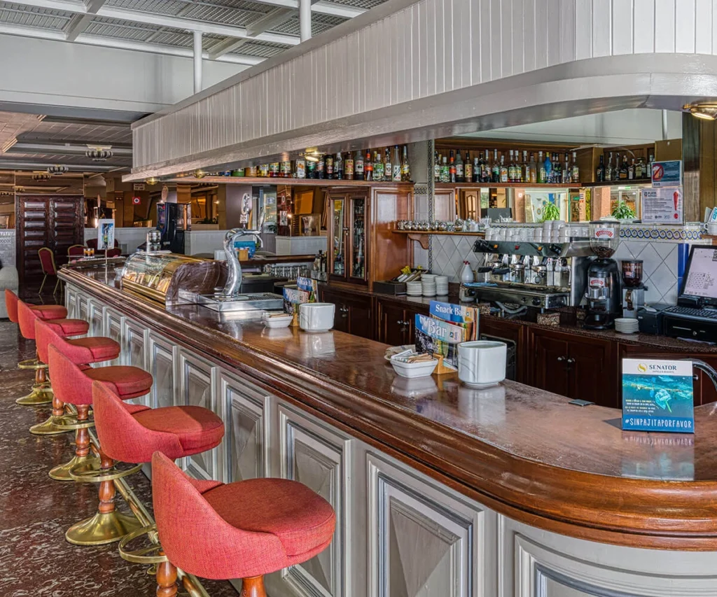 Barra de bar con bebidas, cafeteras y sillas rojas en interior industrial
