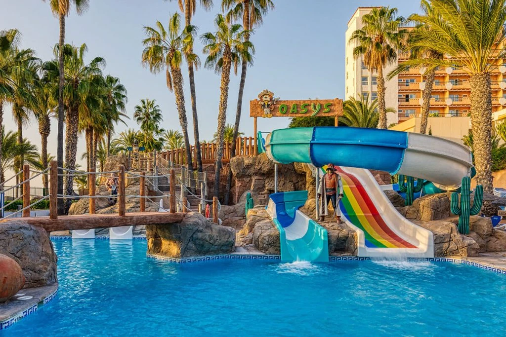 Tobogán acuático con piscina y palmeras junto a un hotel en Oasis.