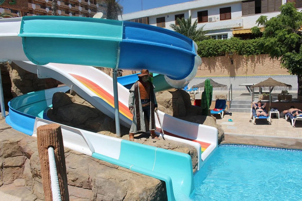 Tobogán acuático azul y verde con bañistas en una piscina junto a rocas