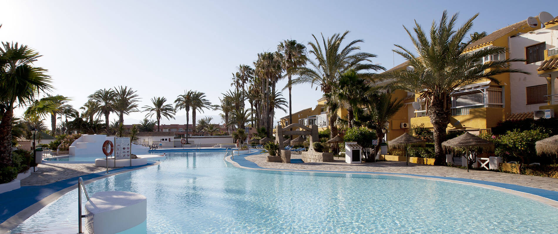 Piscina de hotel con palmeras y edificios junto a un cielo despejado