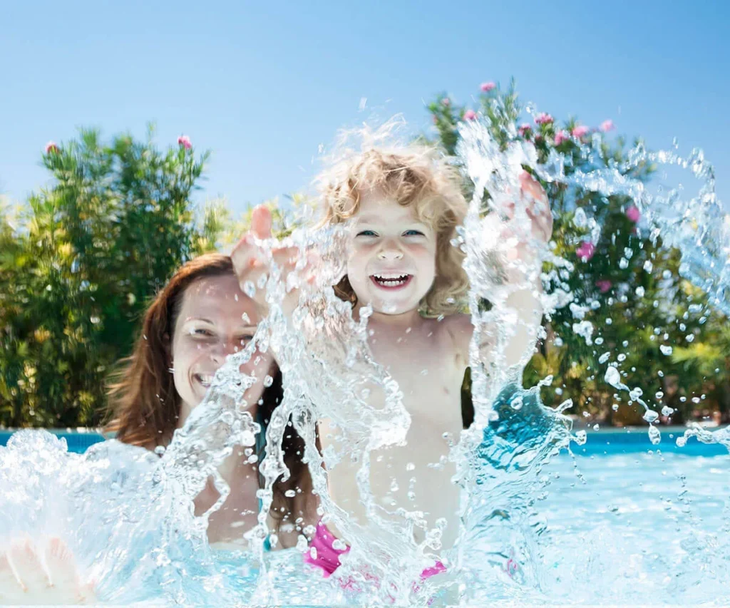 Ni&ntilde;os jugando en una piscina con agua a chorros y flores al fondo