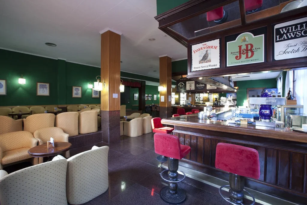 Bar con taburetes rojos, asientos beige y botellas de whisky en vitrina interior