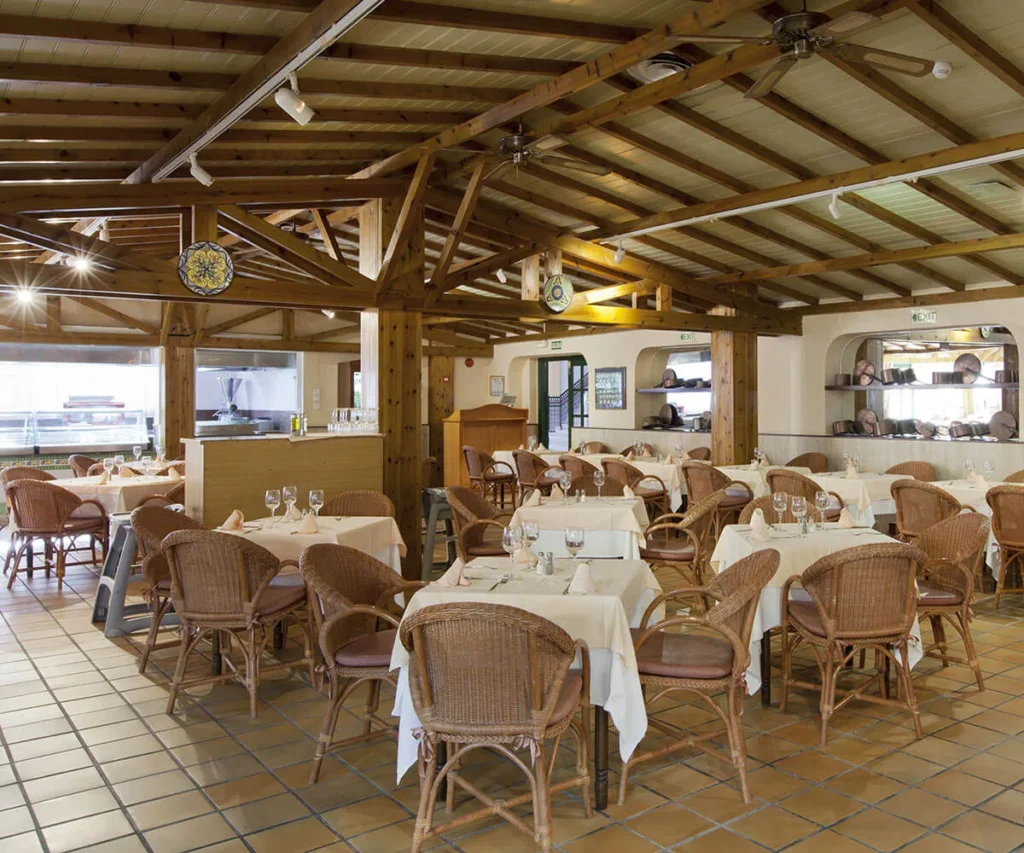 Comedor con mesas servidas, sillas de mimbre y techo de madera con vigas y l&aacute;mparas
