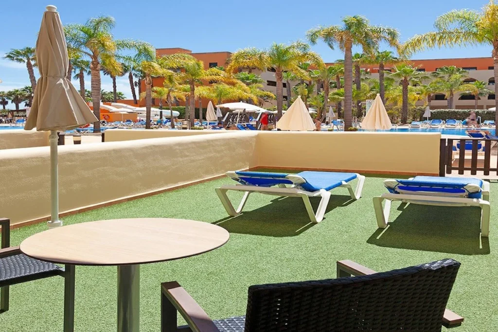 Terraza de hotel con c&eacute;sped sint&eacute;tico, tumbonas azules y palmeras al sol