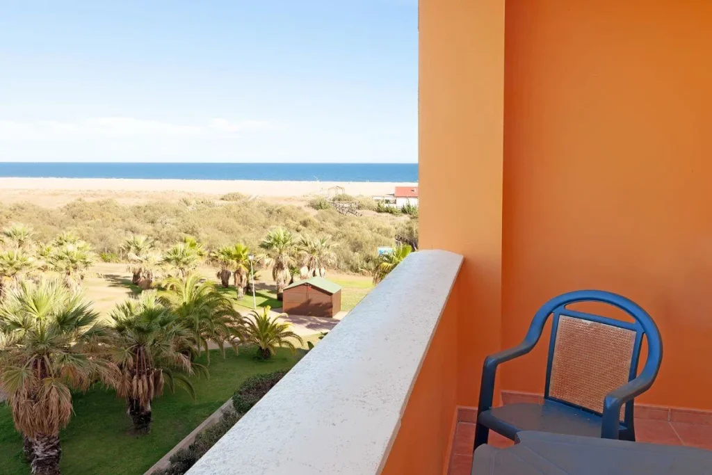Balcon naranja con silla y vista al mar y palmeras, desde la terraza
