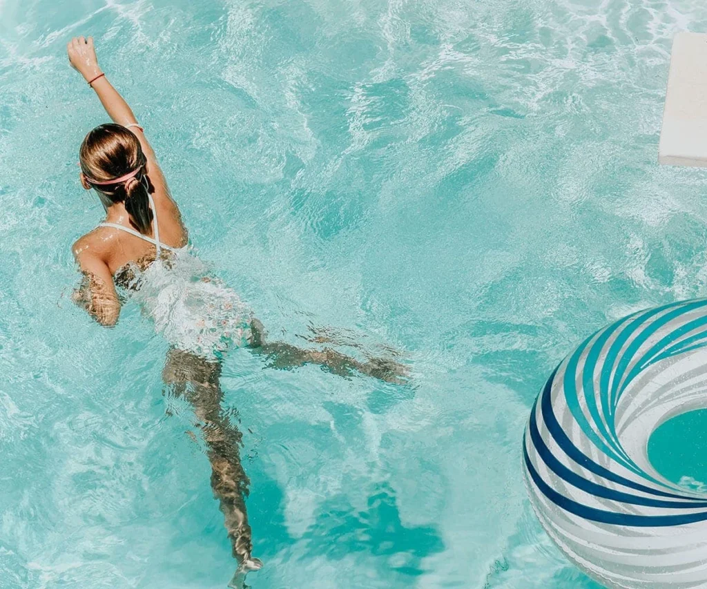Mujer nadando en una piscina turquesa con flotador a rayas