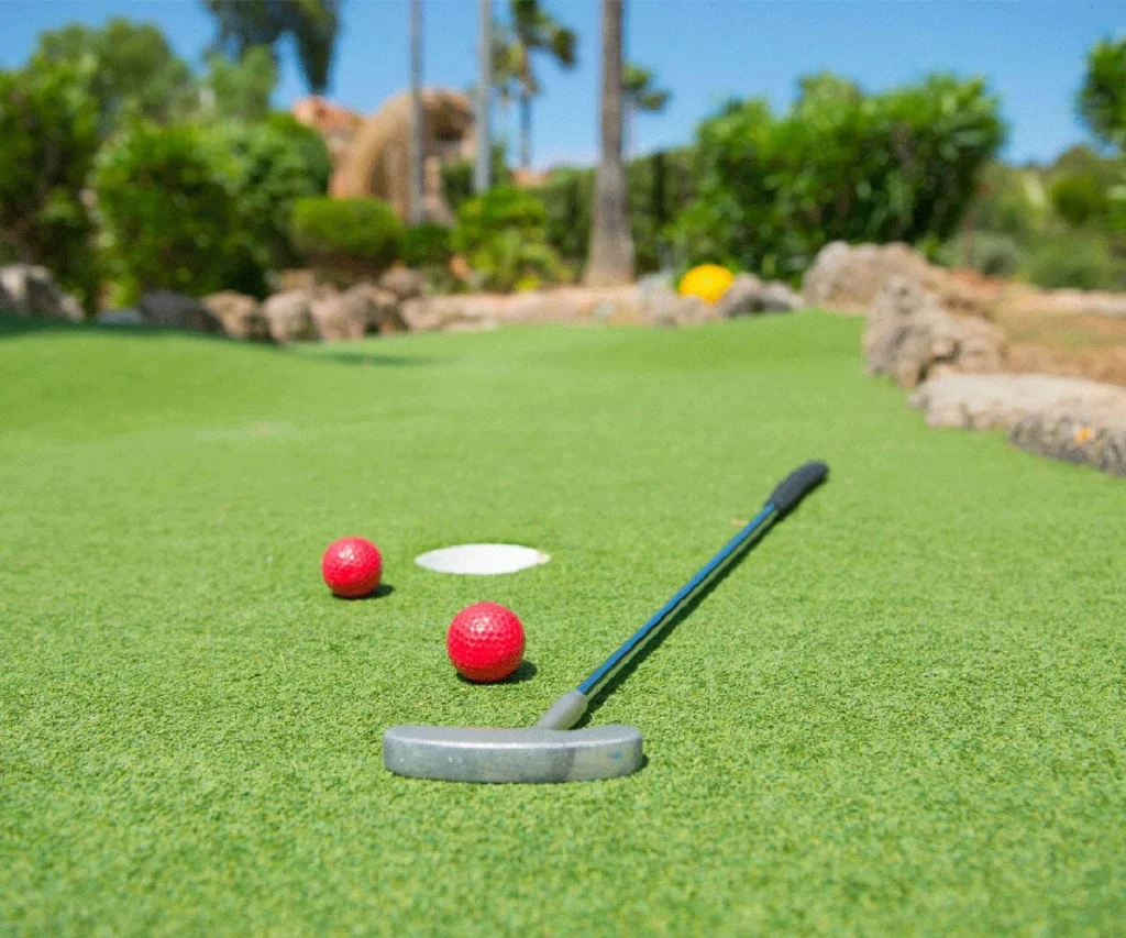 Palos y pelotas rojas sobre una cancha verde de minigolf al aire libre