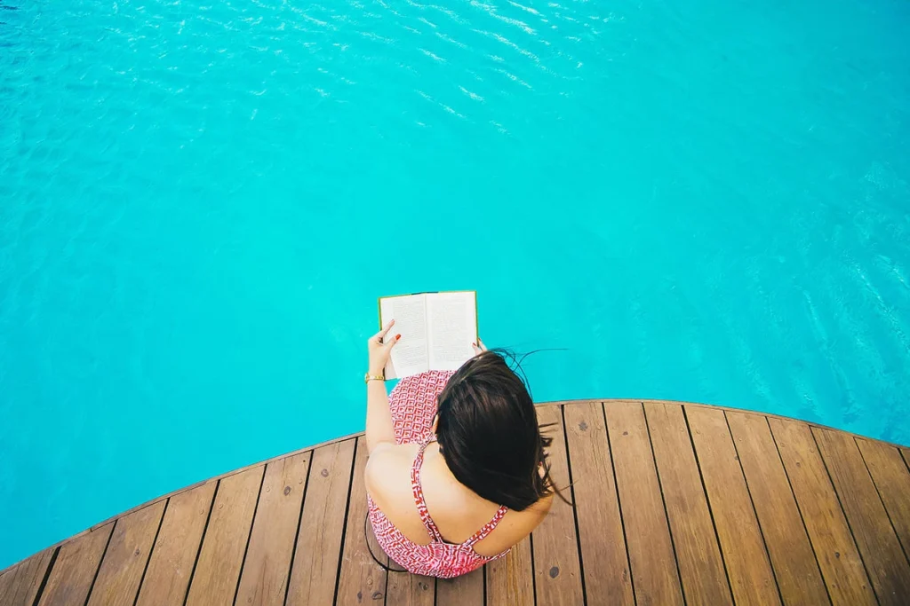 Mujer leyendo un libro con la espalda al borde de una piscina azul