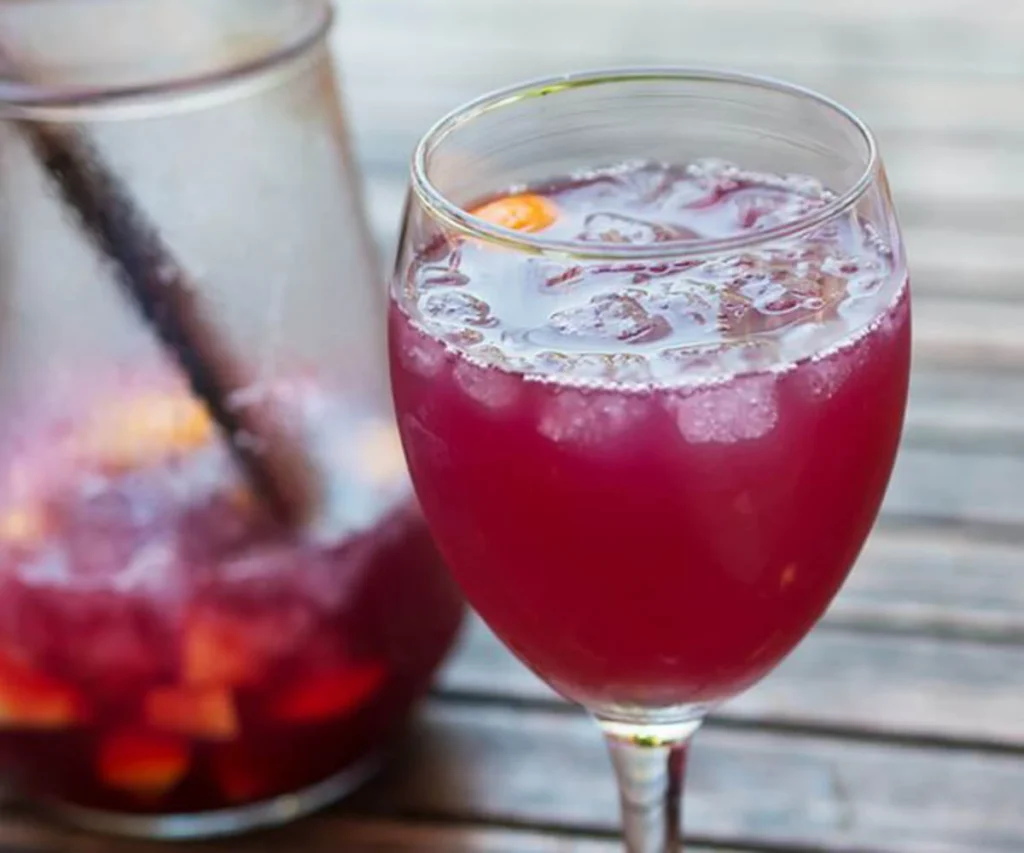 Vaso con bebida roja burbujeante con hielo sobre mesa de madera clara