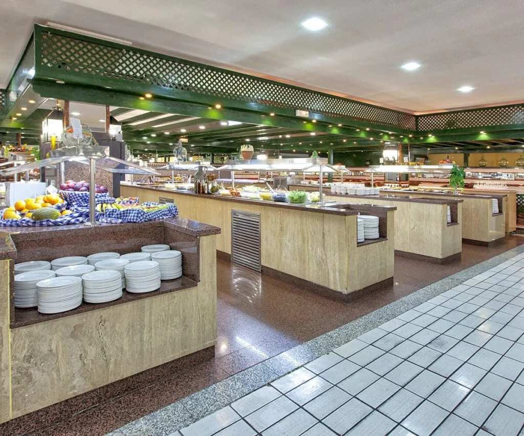 Buffet de hotel con mesas, alimentos y platos apilados en &aacute;rea de comedor