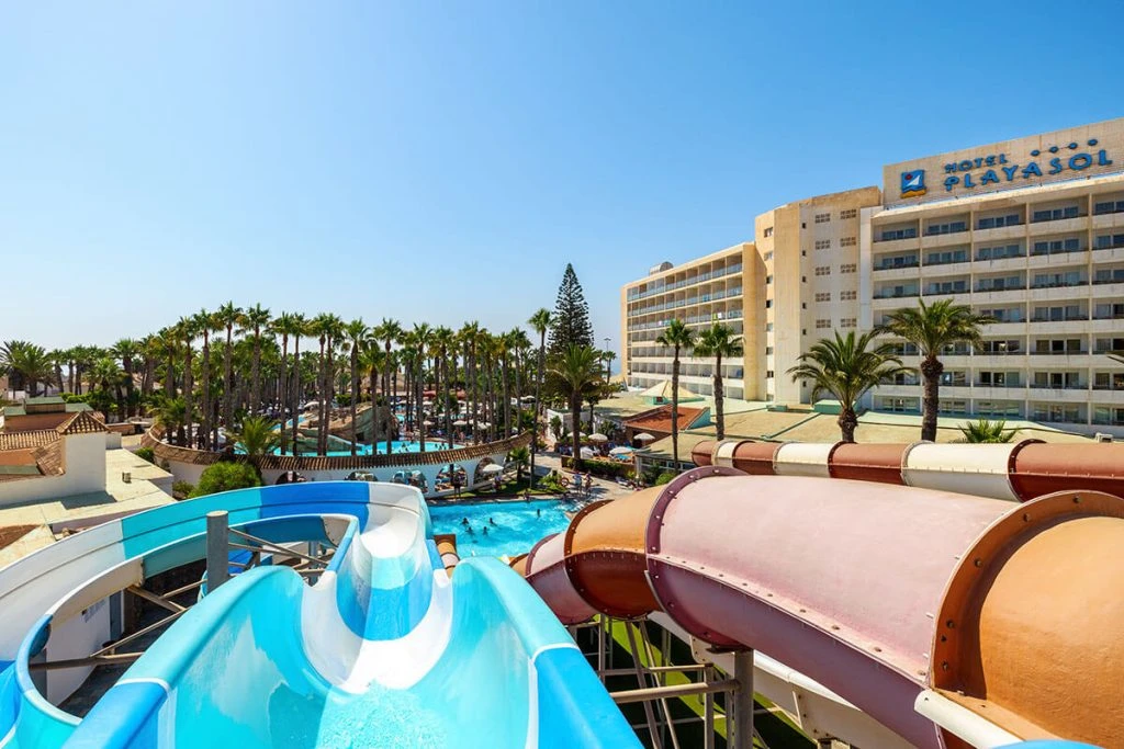 Piscina y toboganes de agua con el Hotel Playa Ásol al fondo, cielo azul