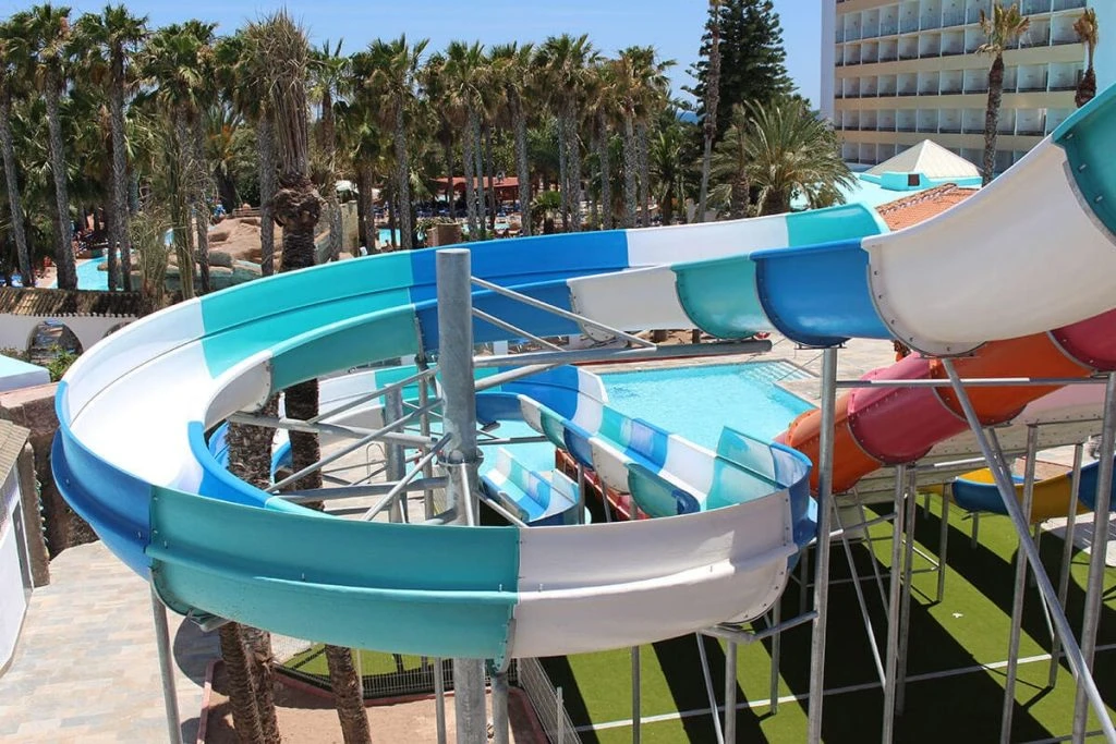 Toboganes acuáticos y piscina junto a palmeras en un hotel.