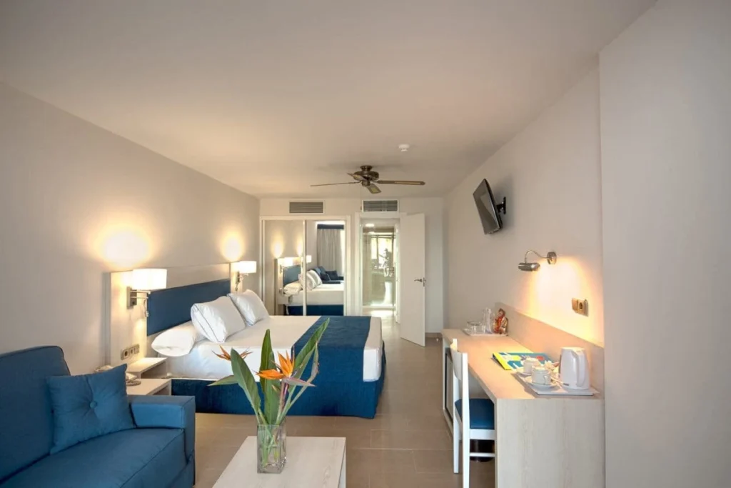 Habitaci&oacute;n de hotel con cama doble, sof&aacute;, mesa y balc&oacute;n.