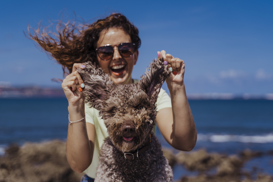 young woman and her cute spanish water dog outdoors enjoying together at the beach