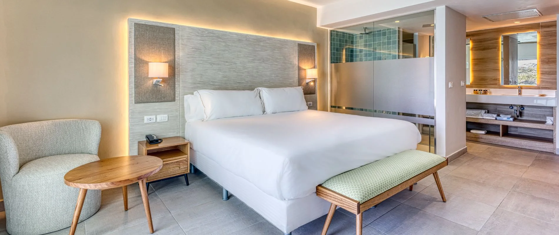 Habitaci&oacute;n de hotel moderna con cama doble, mesitas y ba&ntilde;o integrado.