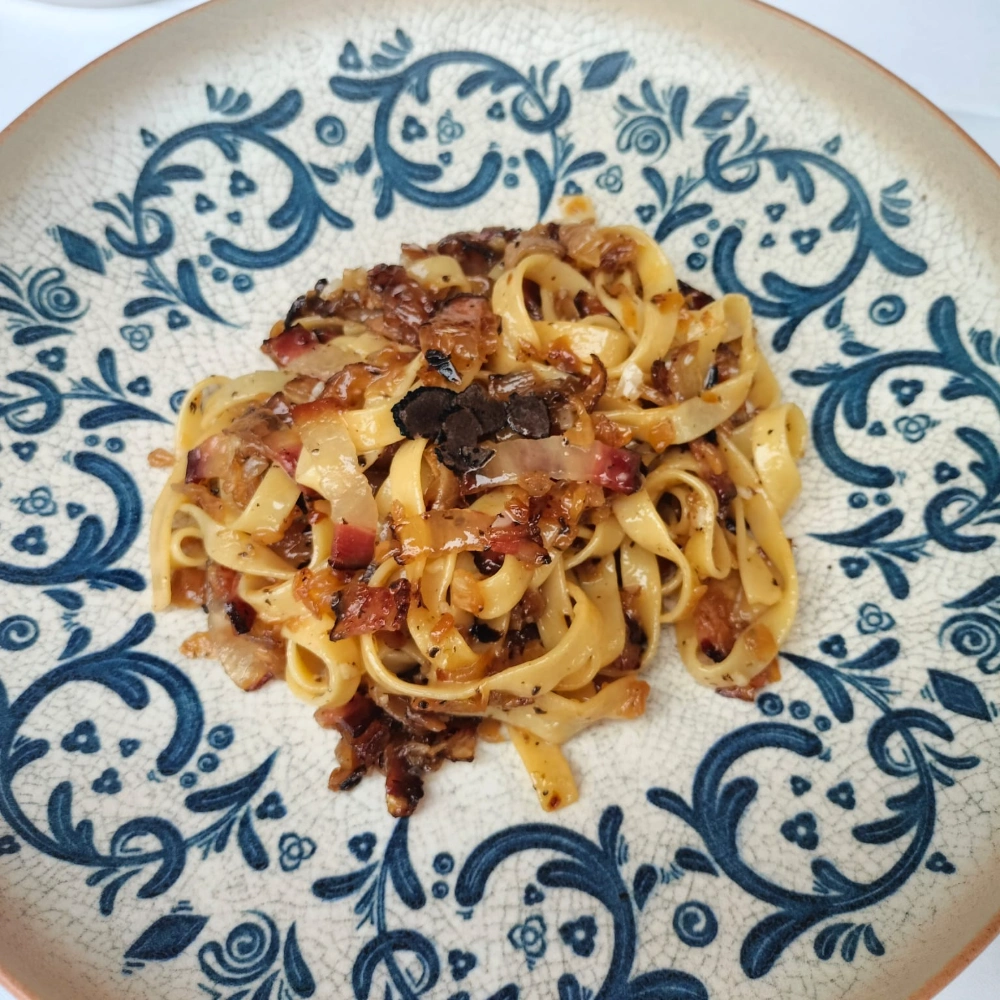 Plato de pasta con salsa y guarnici&oacute;n en un plato decorativo azul.