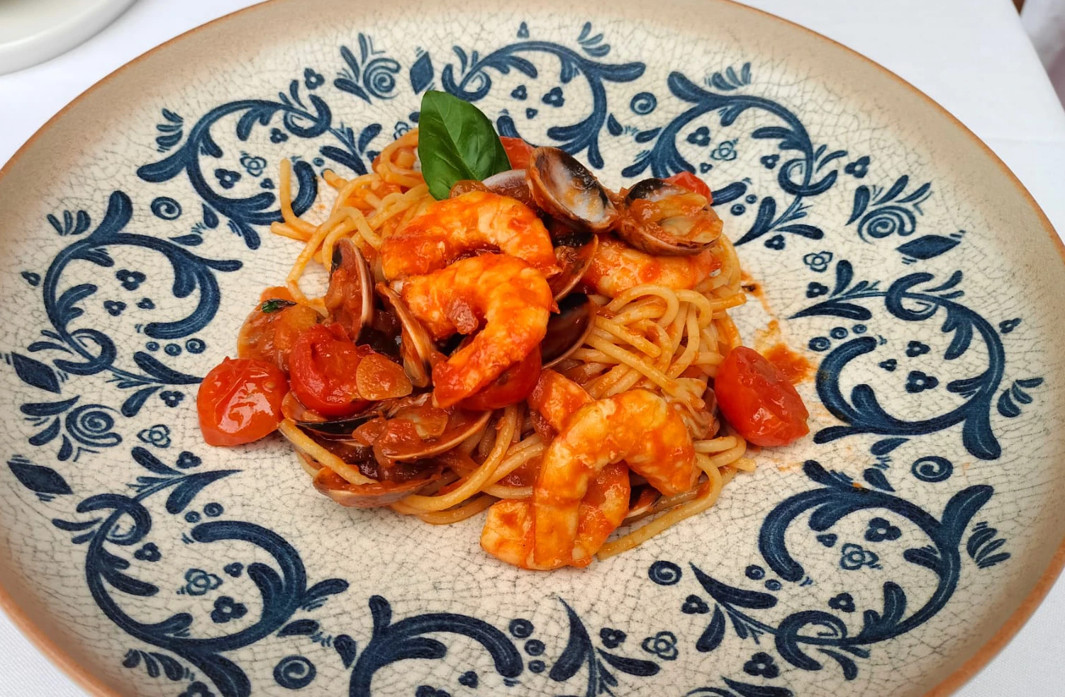 Plato de espaguetis con camarones, almejas y tomates en una fuente decorada.