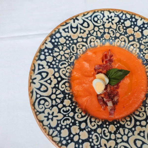 Plato decorado con sopa anaranjada, huevo, jam&oacute;n y hoja verde.