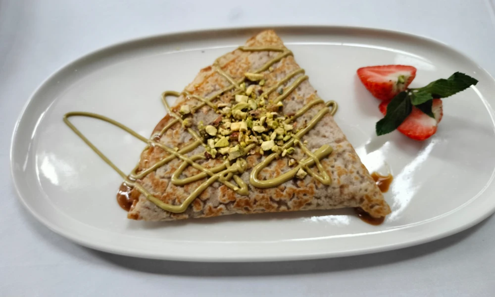 Crepa con crema de pistacho y fresas en un plato blanco ovalado.