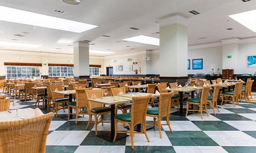 Restaurante amplio con mesas y sillas de mimbre y piso de cuadros.