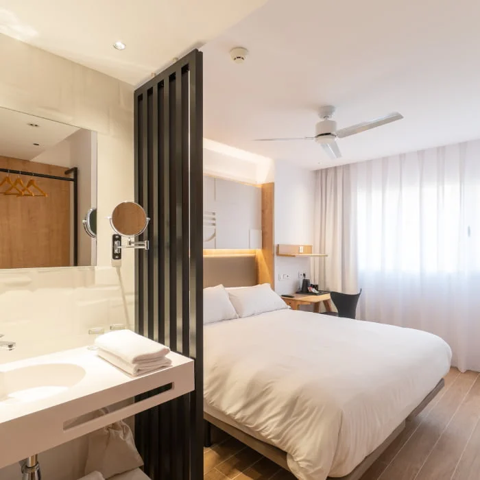 Habitaci&oacute;n de hotel moderna con cama, cortinas y ventilador de techo.