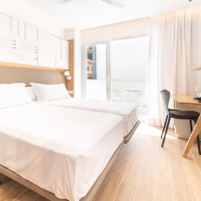 Habitaci&oacute;n hotelera luminosa con cama doble, escritorio y cortinas claras