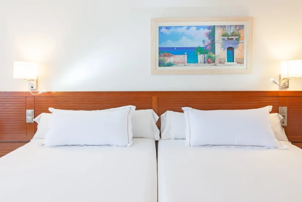 Dormitorio con dos camas, almohadas blancas y un cuadro de pared