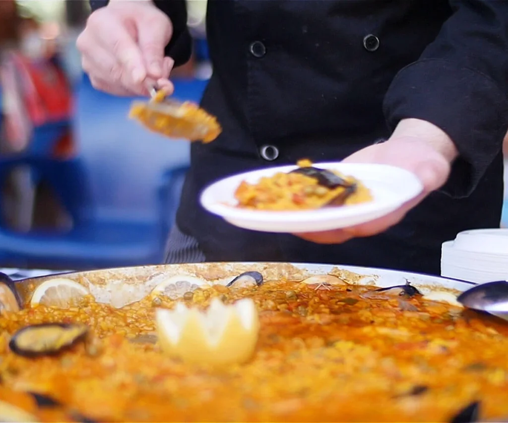 Cocinero sirve un plato de paella con cuchara y guisos en la mesa
